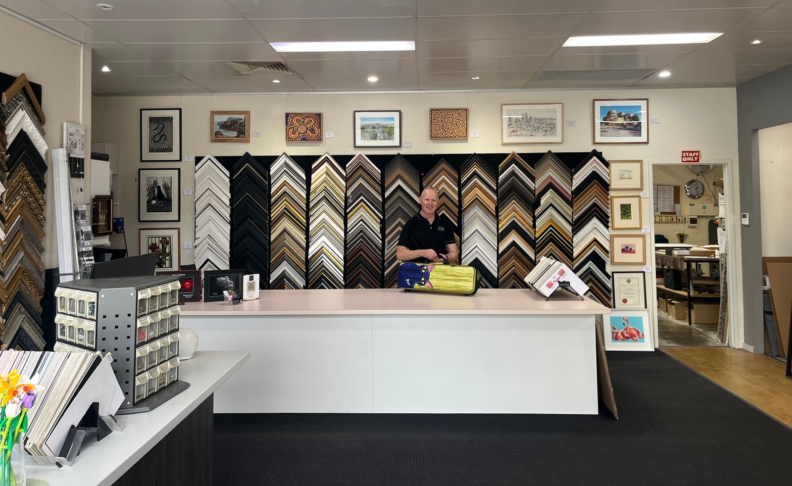 A team member at the showroom counter, with frame samples displayed behind him